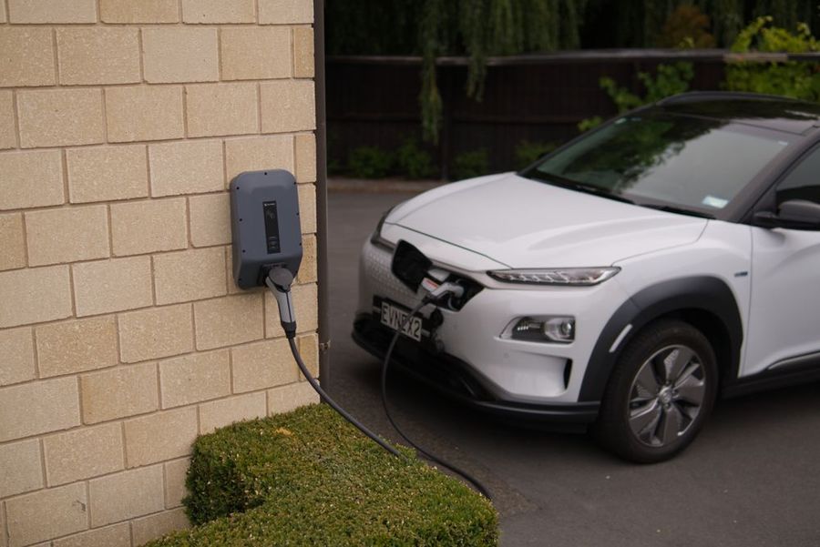 A white electric car charging at a wall-mounted charge point