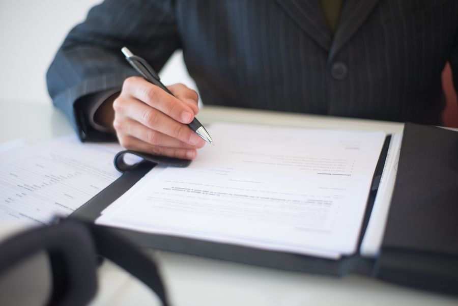 Someone in a suit signing a document on a clipboard