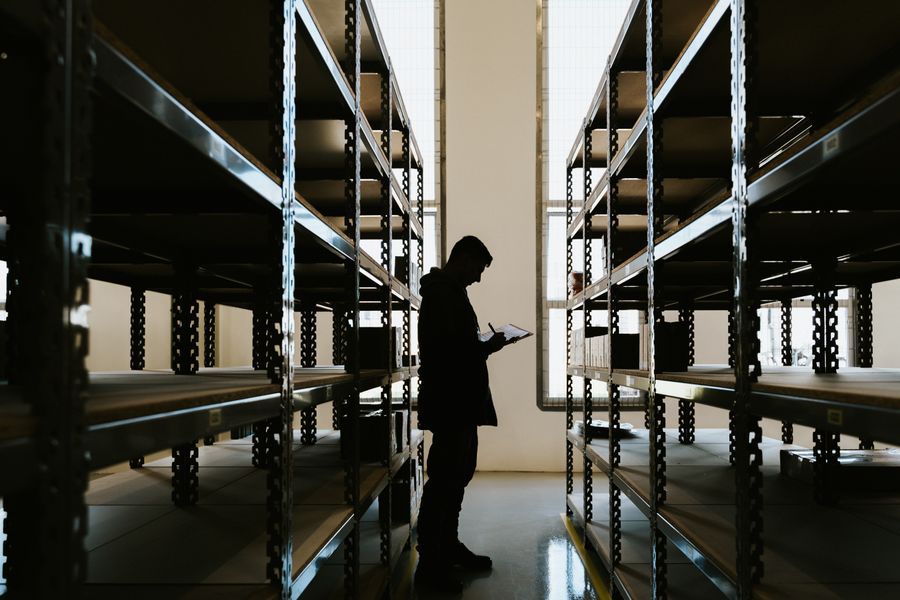 A person walking between tall empty racking in a warehouse aisle