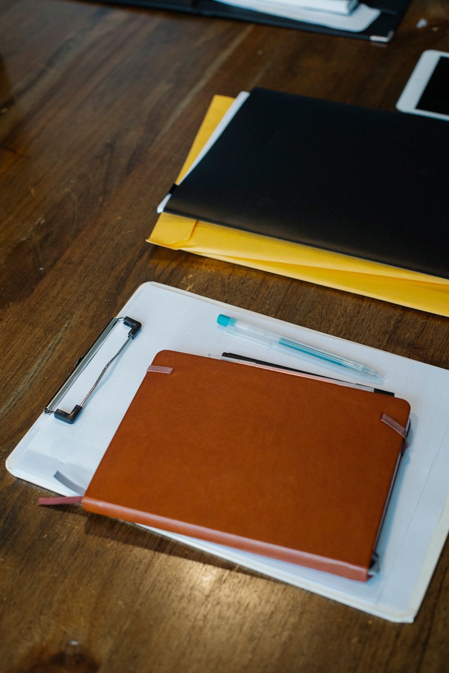 A leather folder, notebooks and a pen laid out on a wooden desk