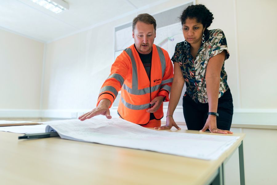 Two people in a site office reviewing a large technical drawing on a table