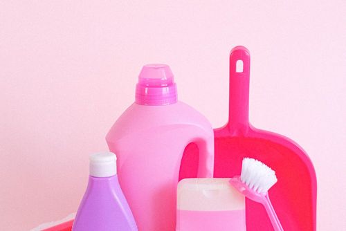 Pink cleaning bottles with a dustpan and a scrubbing brush