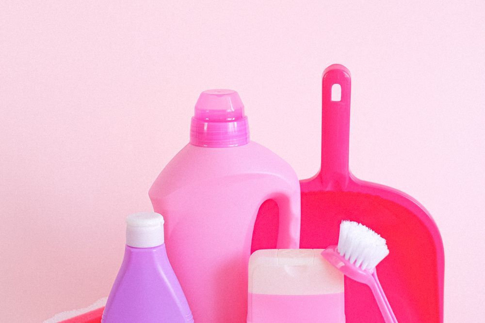 Pink cleaning bottles with a dustpan and a scrubbing brush