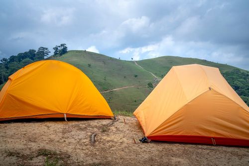 Two orange camping tents pitched on a grassy hillside