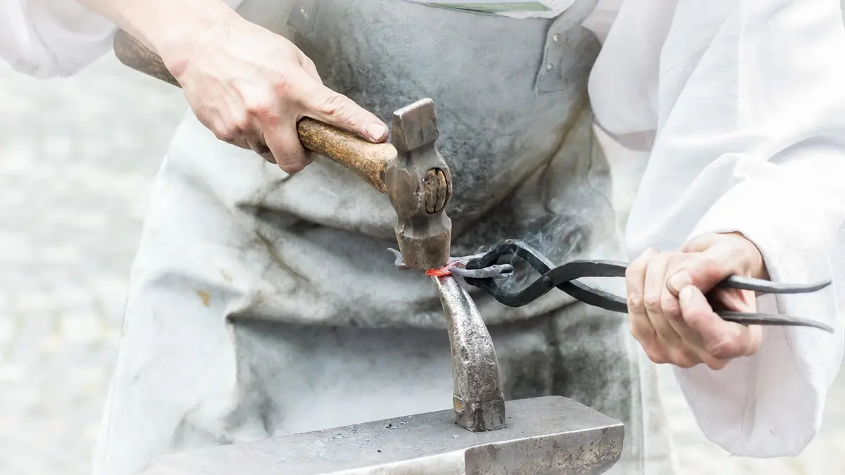 A blacksmith works with iron, a hammer and an anvil at a forge.