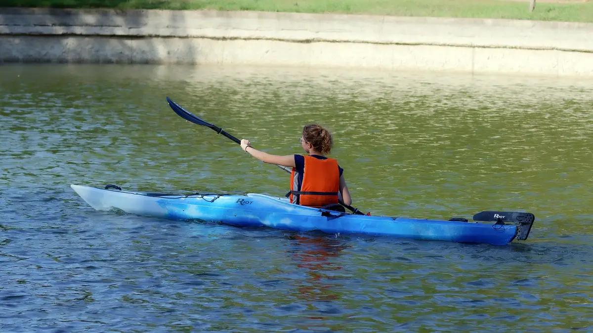 A girl wearing a lifejacket rows a kayak on a lake.