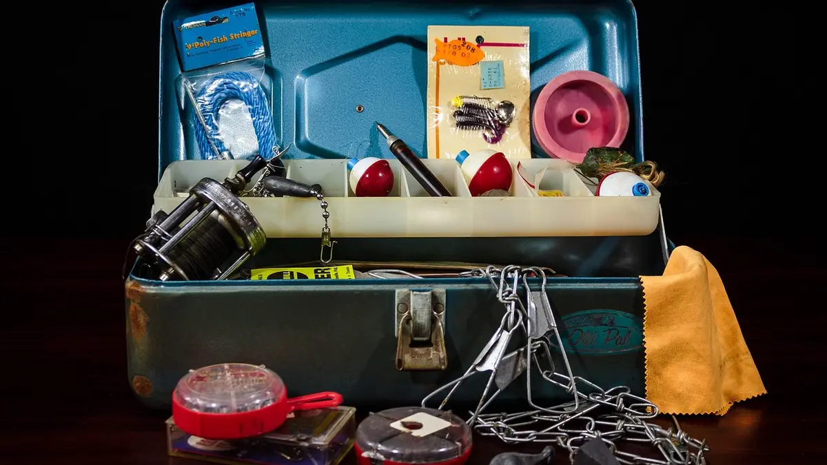 A tackle box with fishing lures, hooks, a reel and fishing line.