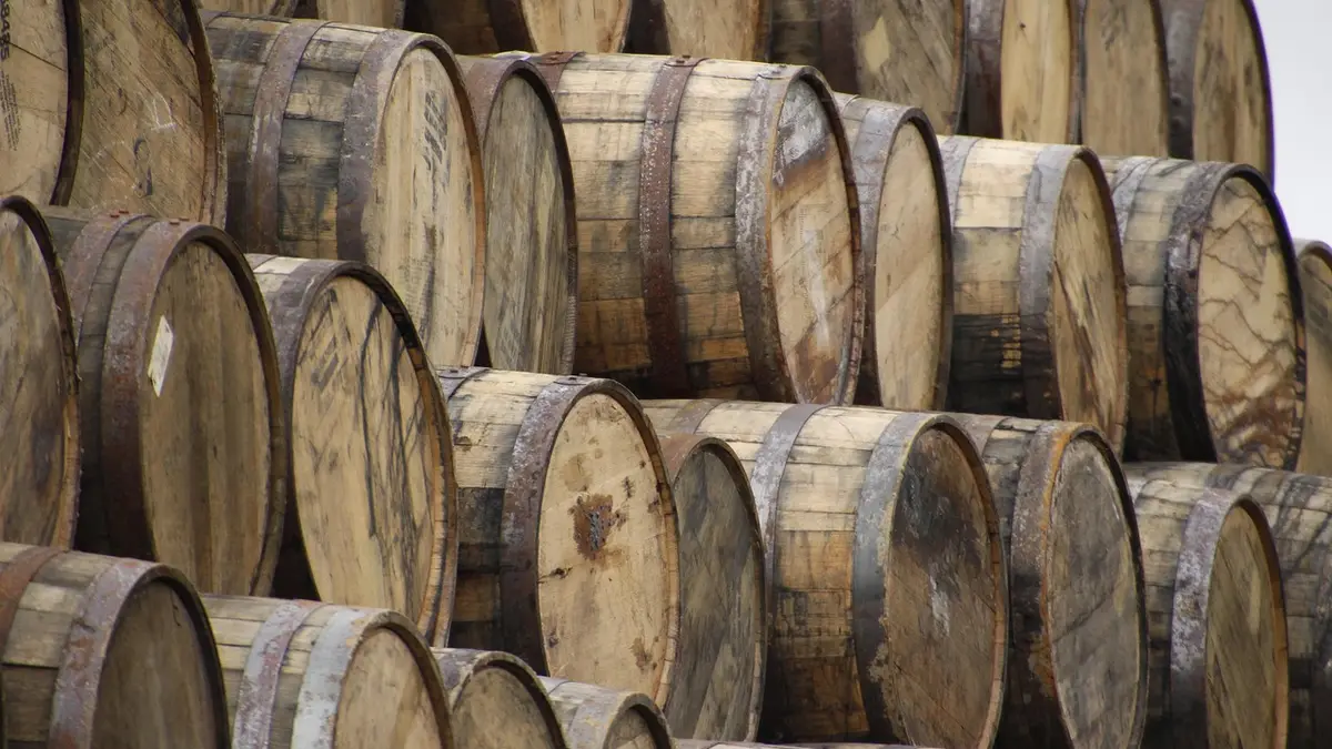 Wooden whiskey barrels stacked in a warehouse.