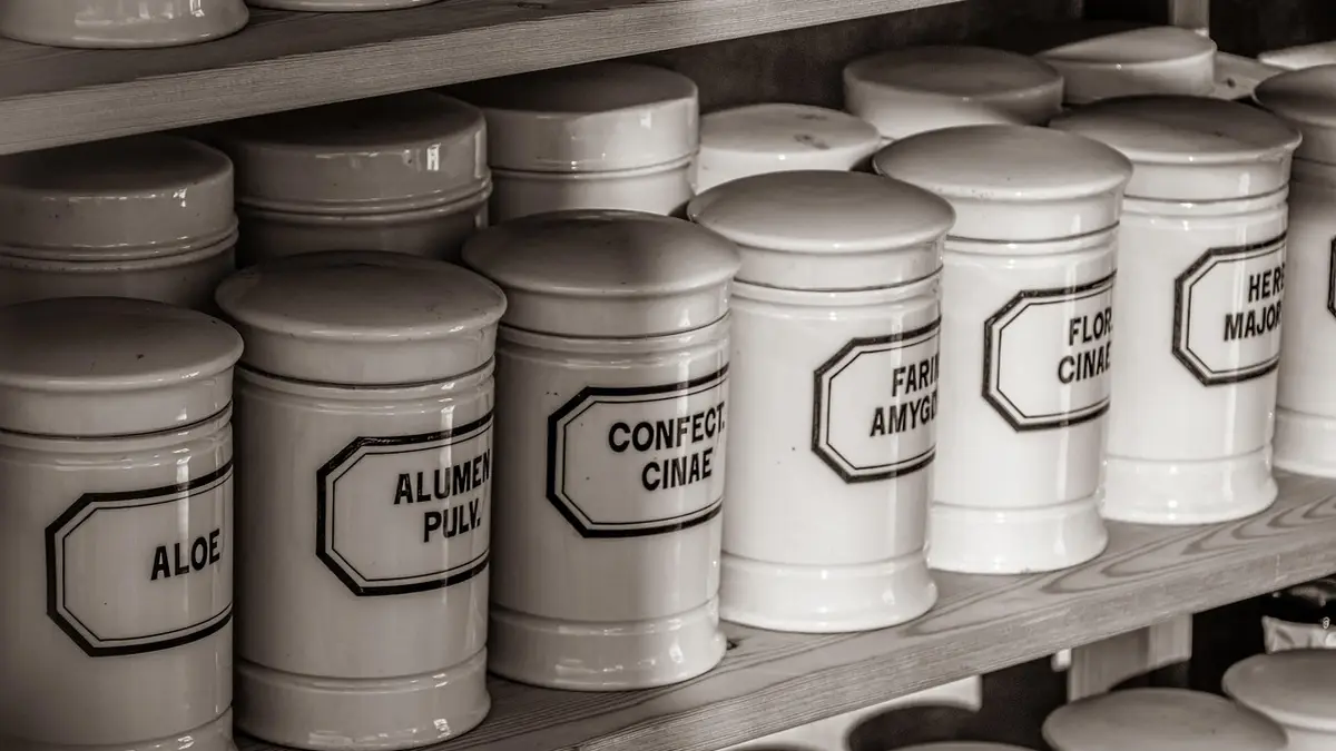Old medicinal bottles sit on a pharmacy cabinet shelf.