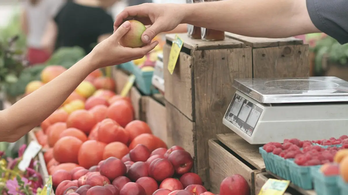 Hands exchange apples at a farmers' market fruit stand.