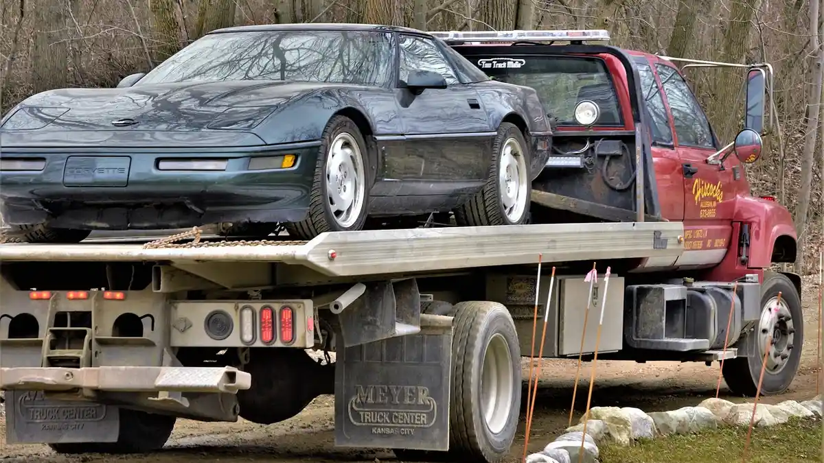 A flatbed truck hauling a broken Corvette sports car.