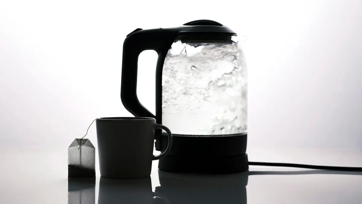 An electric kettle with boiling water and a cup of tea.