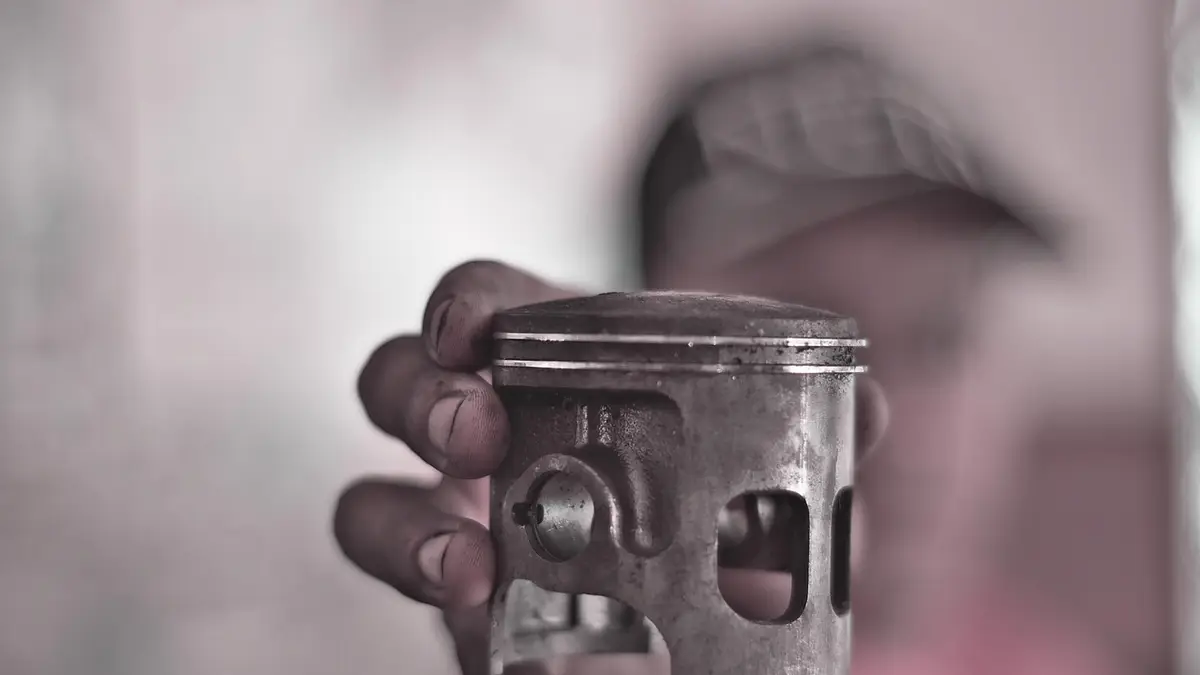 A hand holds an engine piston with rings in a workshop.