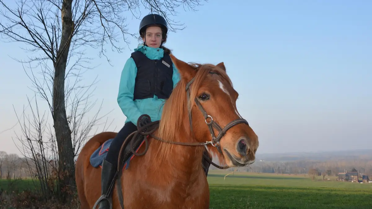 A woman riding a horse wearing a helmet and protective vest.