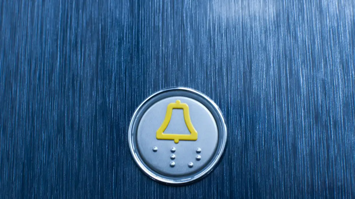 A hand pressing a button on an elevator control panel.