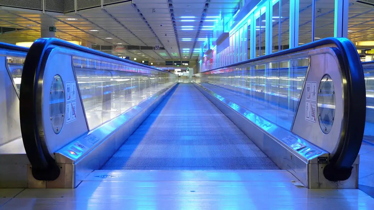 An airport moving walkway with metal segments, handrails and blue lighting.