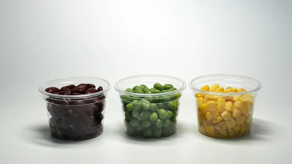 A clear plastic bowl containing sweetcorn, red beans and green peas.