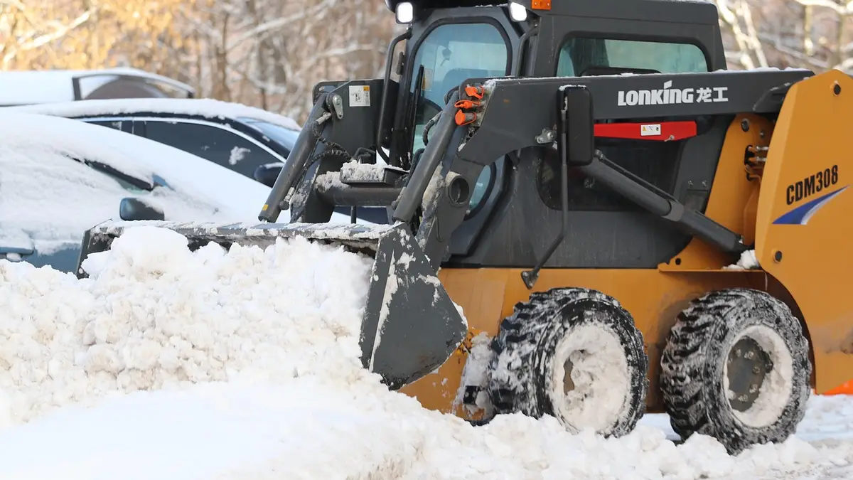 A skid steer loader clearing snow in a yard.