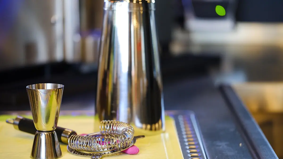 A cocktail shaker, measuring cup and sieve at a bar.