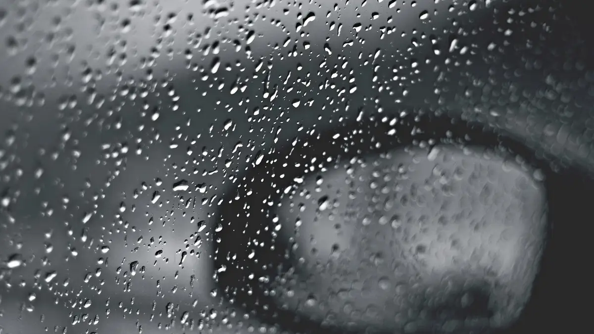 Raindrops on a car window in black and white.