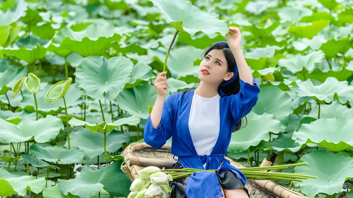 一位穿着吊带背心的女性坐在荷花池中的船上。