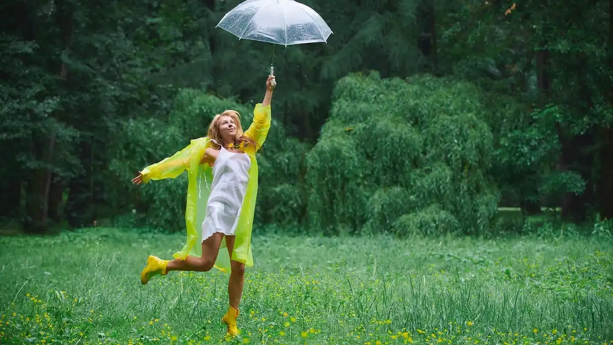A woman in a yellow raincoat and yellow boots in a park.